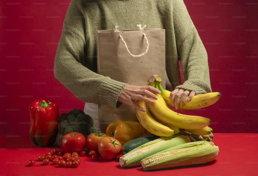 a person holding a bag over a pile of fruit and vegetables