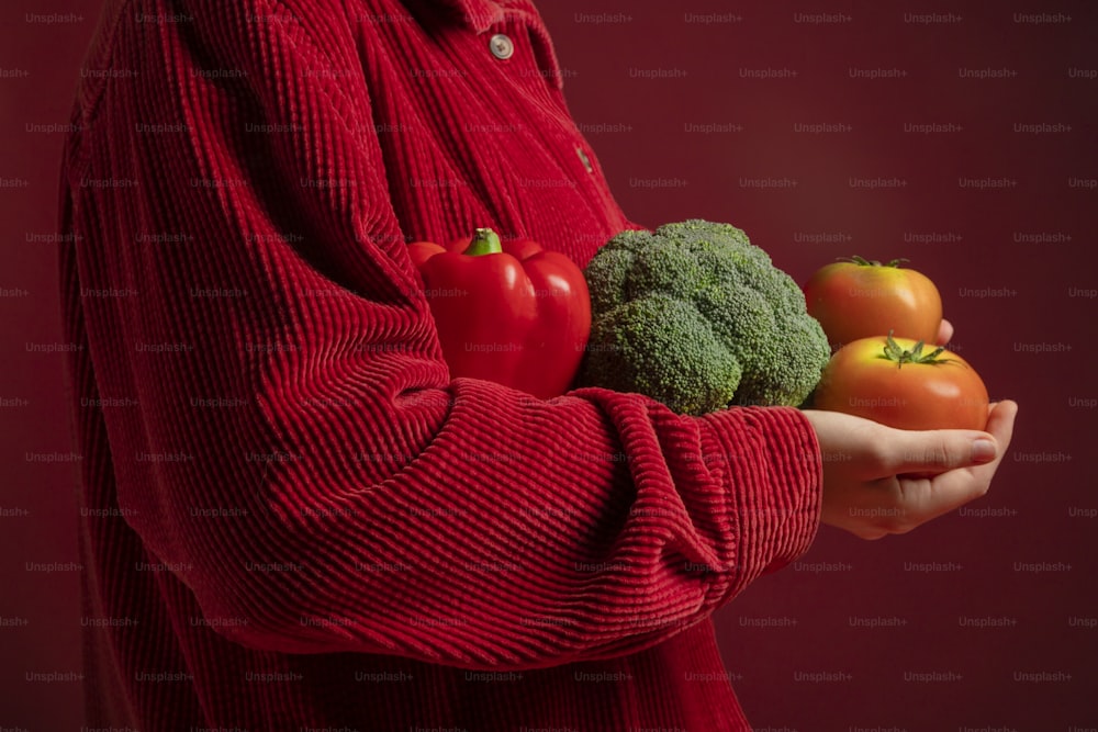 eine Person in einem roten Pullover, die einen Haufen Gemüse in der Hand hält
