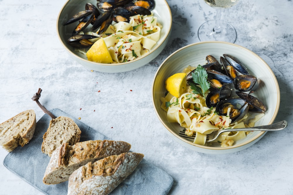 two bowls of pasta with mussels and a glass of wine