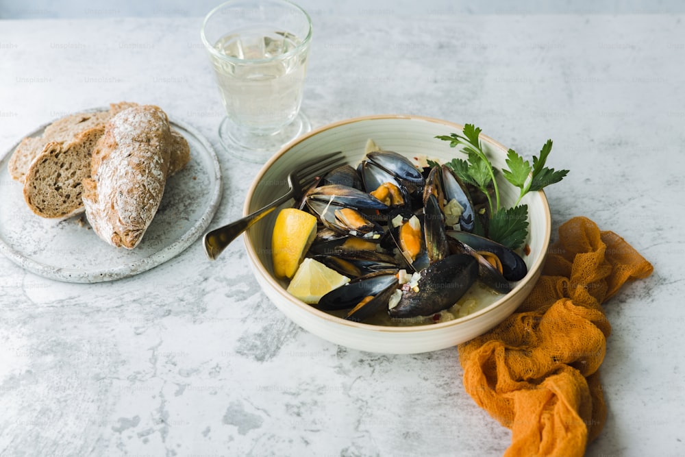 a bowl of mussels next to a glass of water