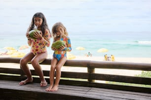 two little girls sitting on a bench at the beach