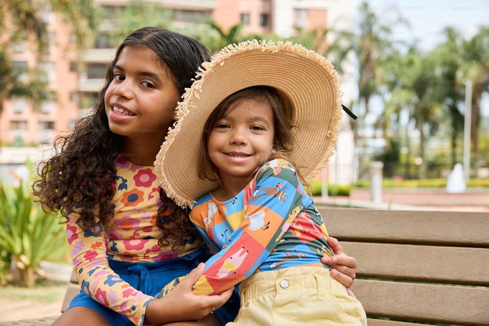 two young girls sitting on a bench wearing hats