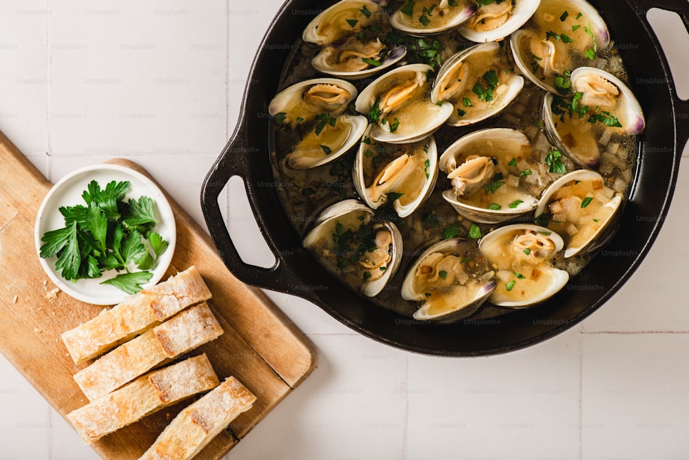 a skillet filled with clams and bread on a cutting board