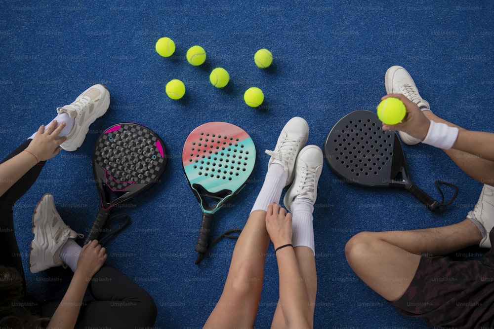 a group of people sitting on the ground with tennis rackets and balls