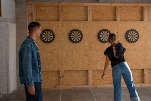 a man and a woman standing in front of a wall with darts on it