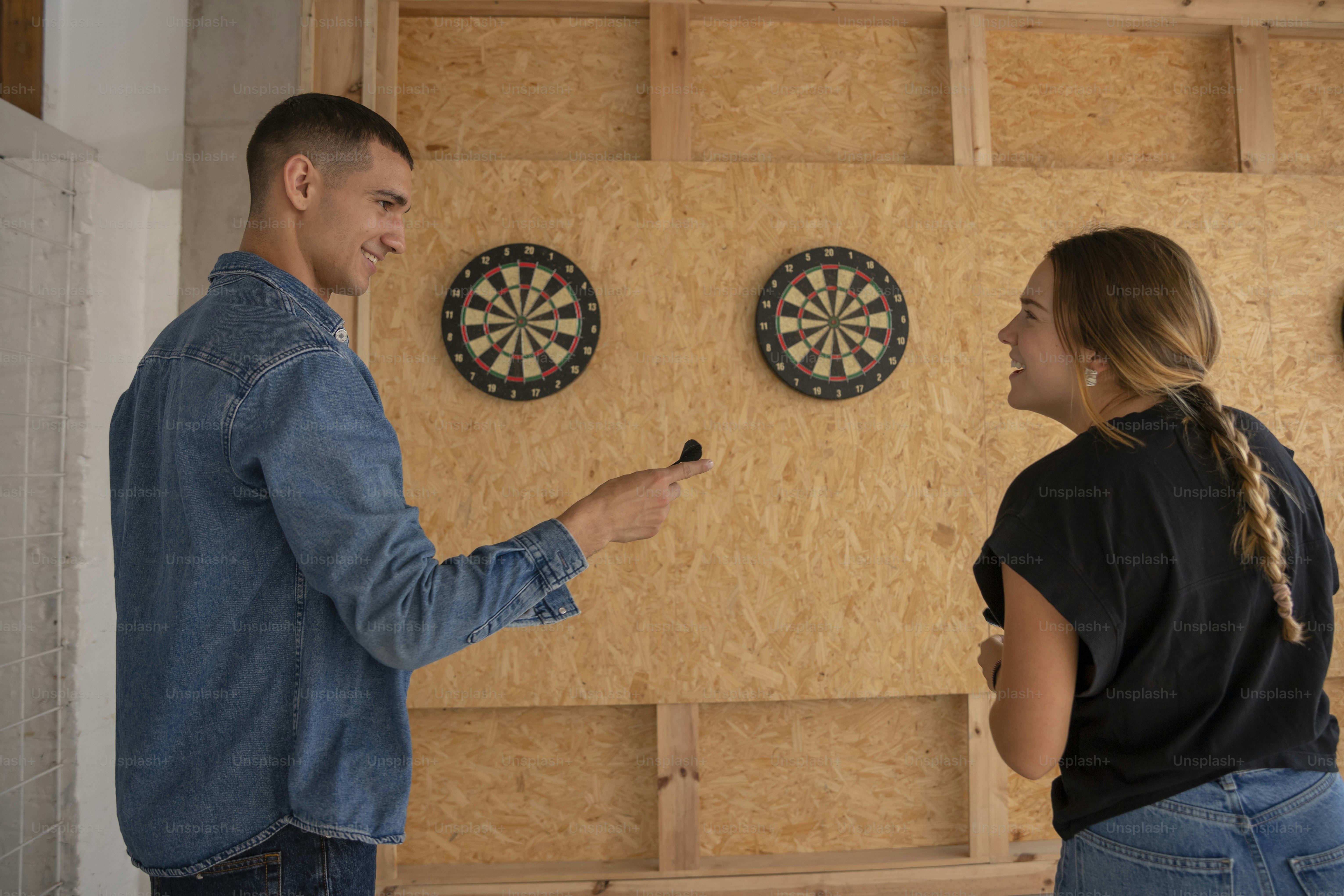 ダーツを載せた壁の前に立つ男女