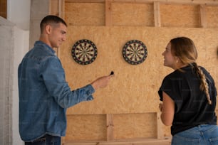 a man and a woman standing in front of a wall with darts on it