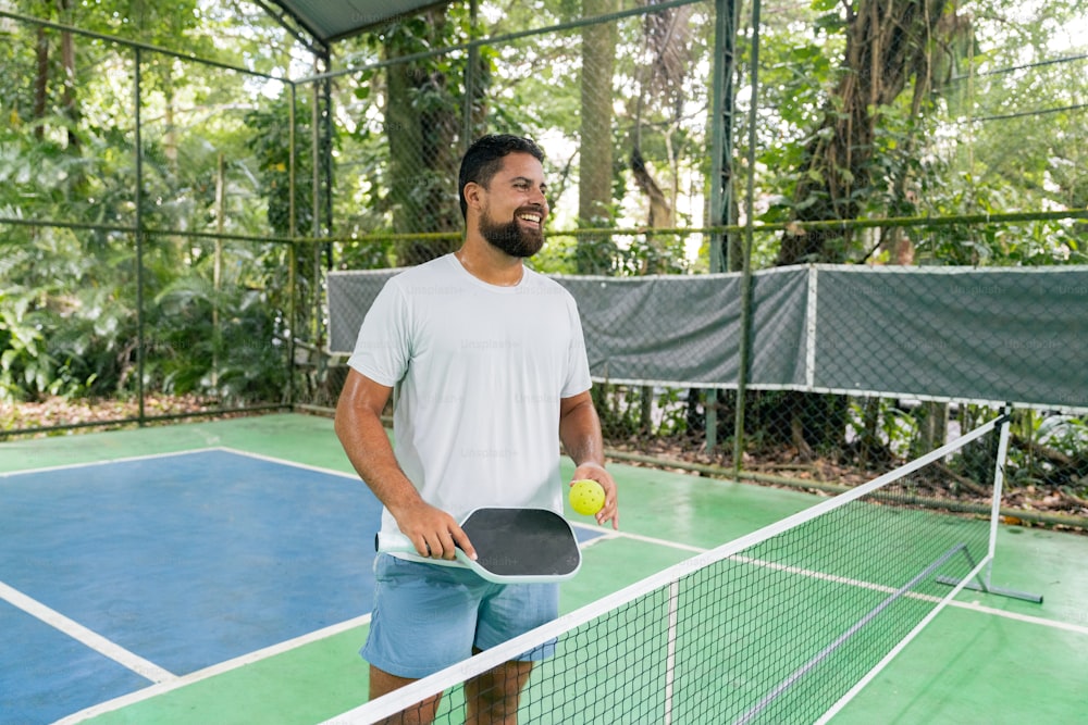 un homme debout sur un court de tennis tenant une raquette et une balle