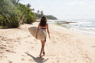 una mujer caminando en una playa con una tabla de surf