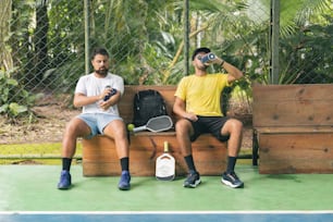 two men sitting on a bench with tennis rackets