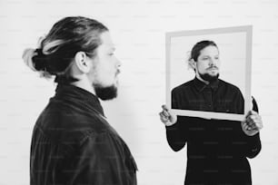 a man holding a picture of himself in front of a mirror