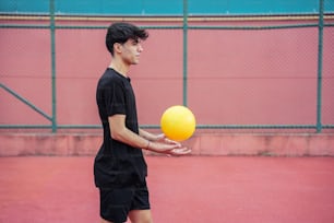 a young man holding a yellow ball on a tennis court
