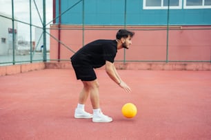a man in black shirt and shorts playing with a yellow ball