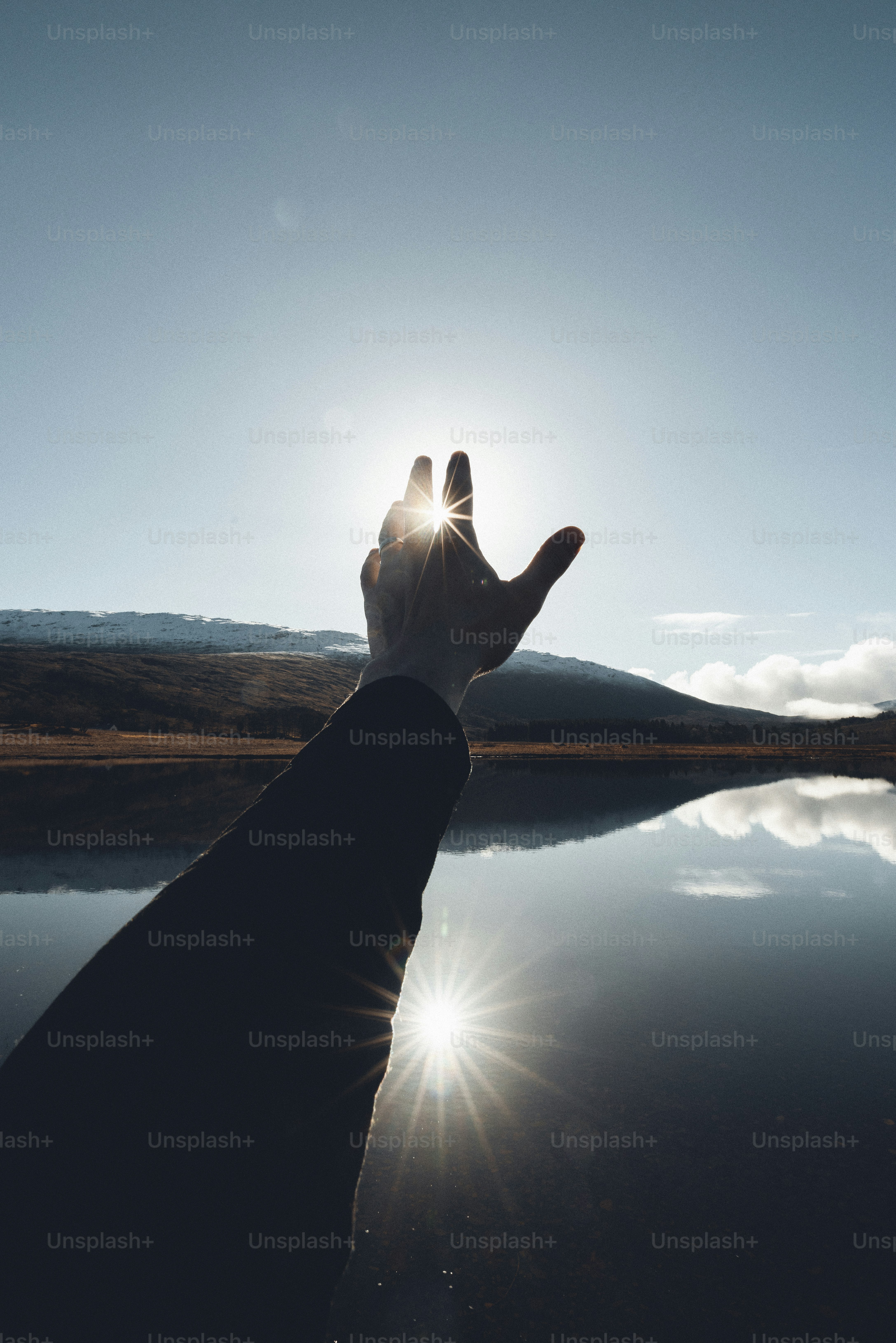 a person's hand reaching out towards the sun