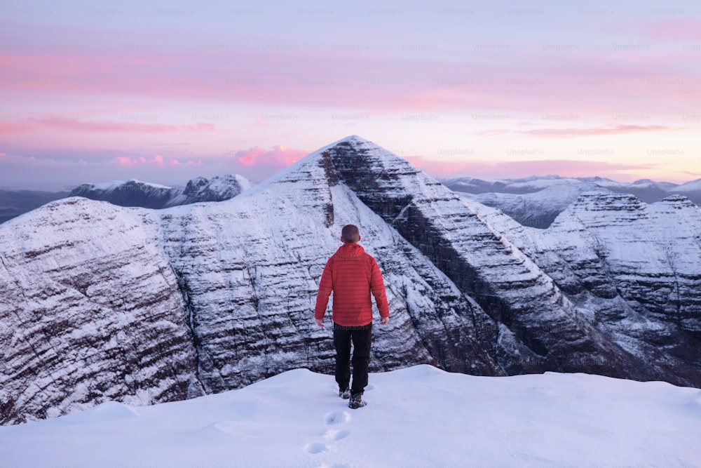 un hombre de pie en la cima de una montaña cubierta de nieve