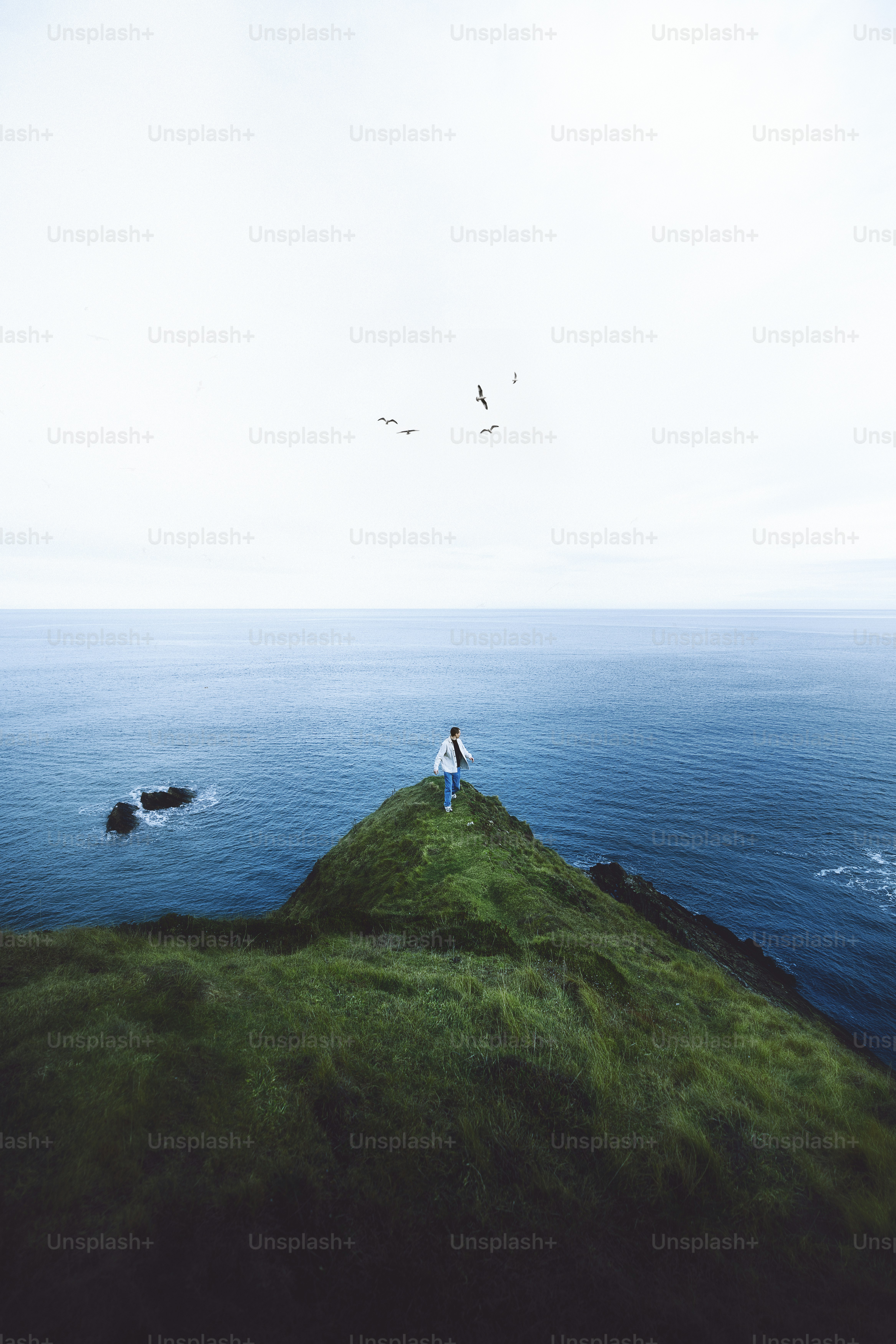 uma pessoa em pé no topo de uma colina coberta de grama ao lado do oceano