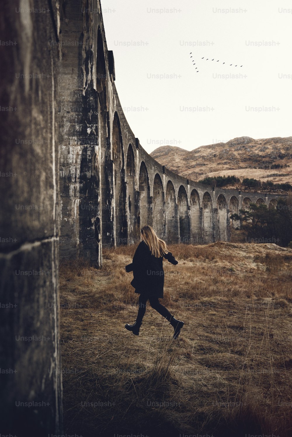 a woman is running in a field near a bridge