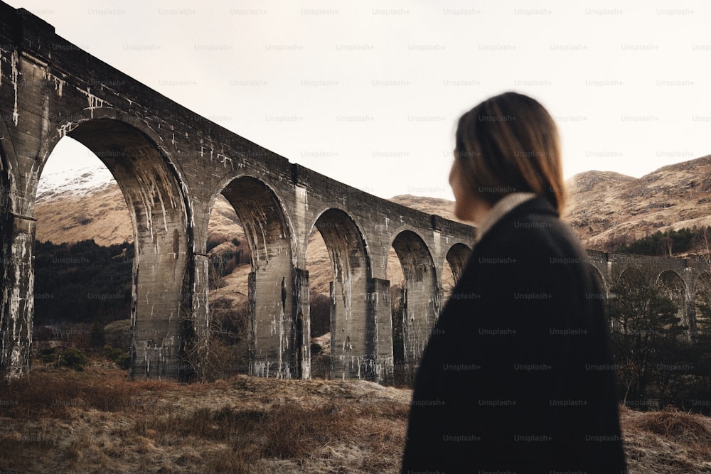 a woman standing in front of an old bridge