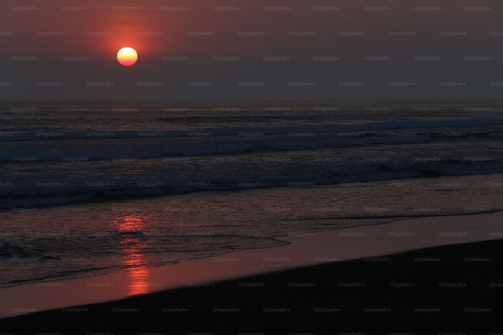 the sun is setting over the ocean on the beach