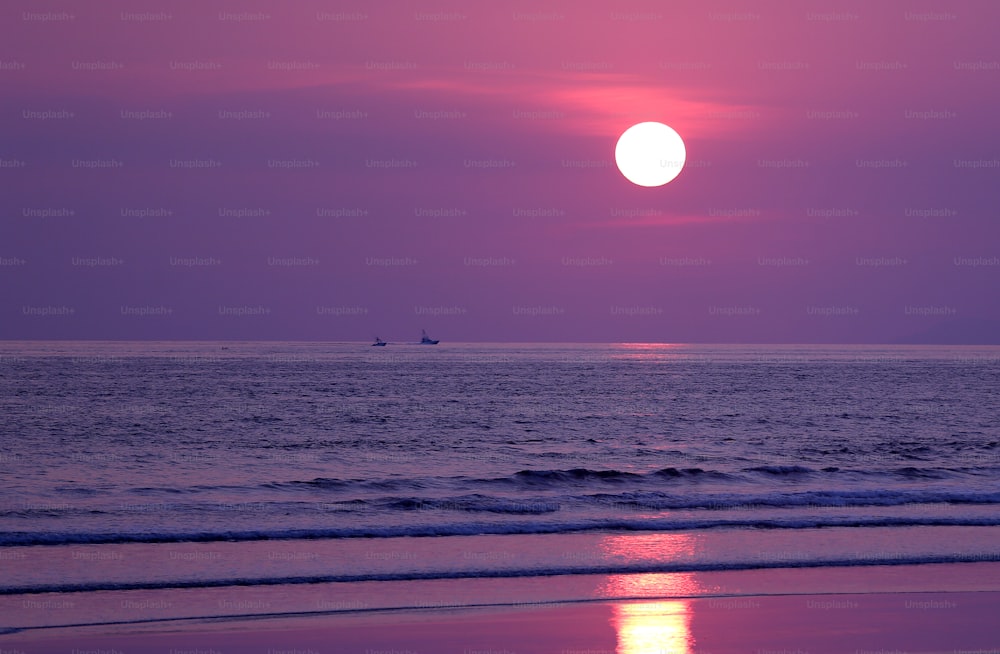 Il sole sta tramontando sull'oceano con una barca in lontananza