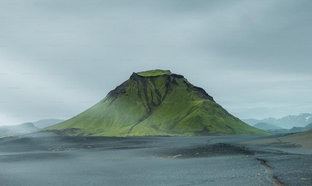 a large green mountain sitting in the middle of a desert