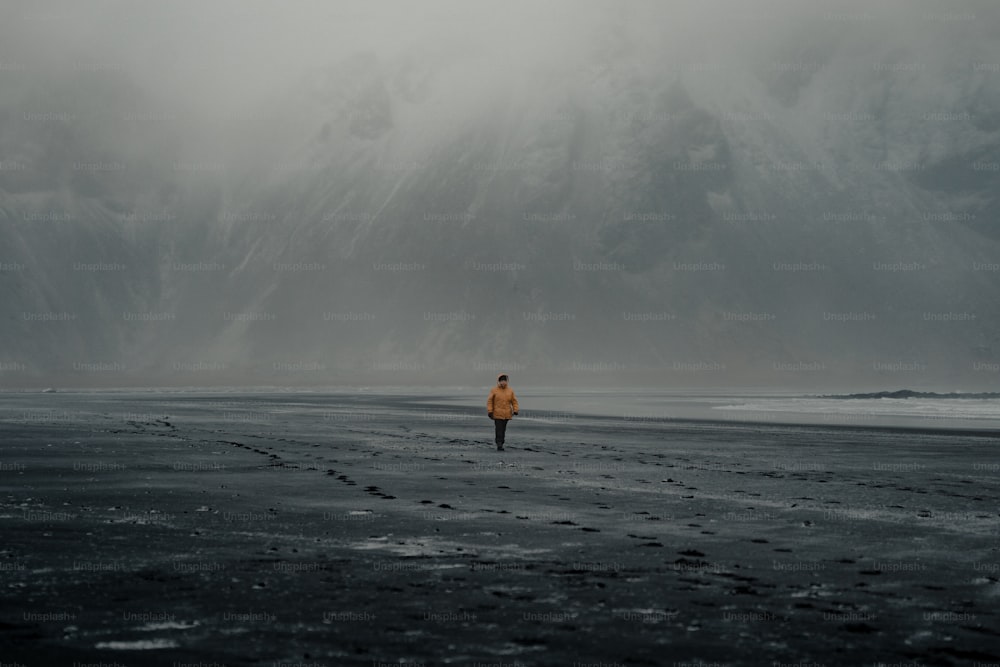 eine Person, die an einem Strand mit Bergen im Hintergrund spazieren geht