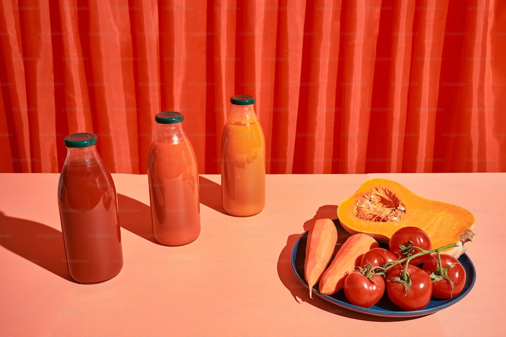 un plato de tomates, zanahorias y una botella de jugo de naranja