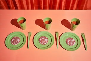 una mesa rosa con platos y utensilios verdes