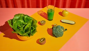 a table topped with a bowl of lettuce next to a glass of juice