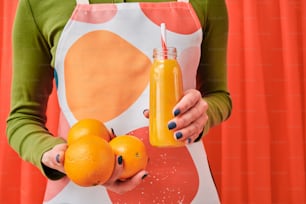 una donna che tiene in mano due arance e una bottiglia di succo