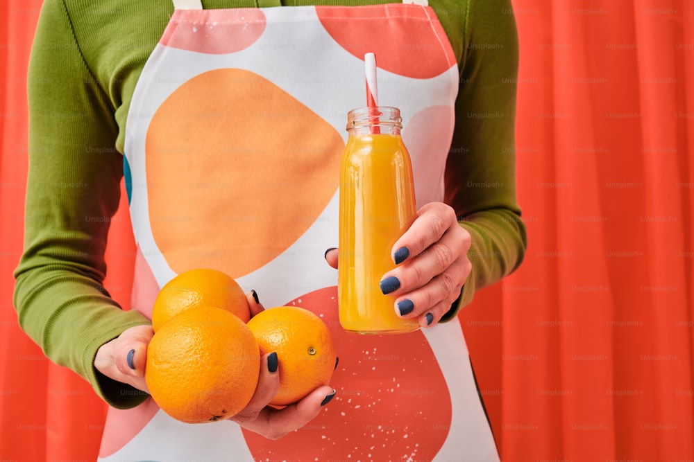 une femme tenant deux oranges et une bouteille de jus