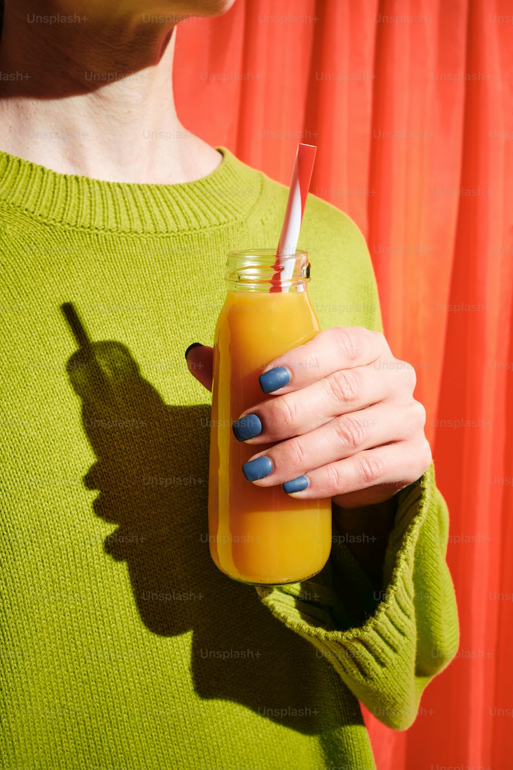 una donna in un maglione verde che tiene in mano un bicchiere di succo d'arancia