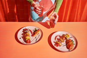 two plates of food on a table with a woman holding a drink