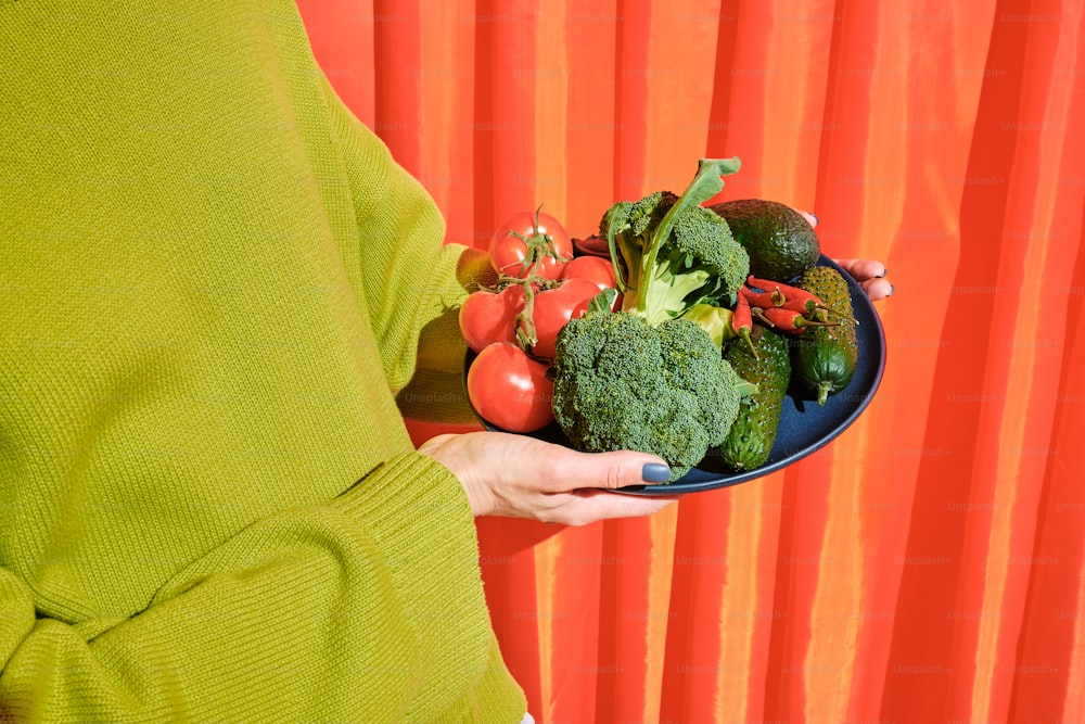 a woman holding a plate of fresh vegetables