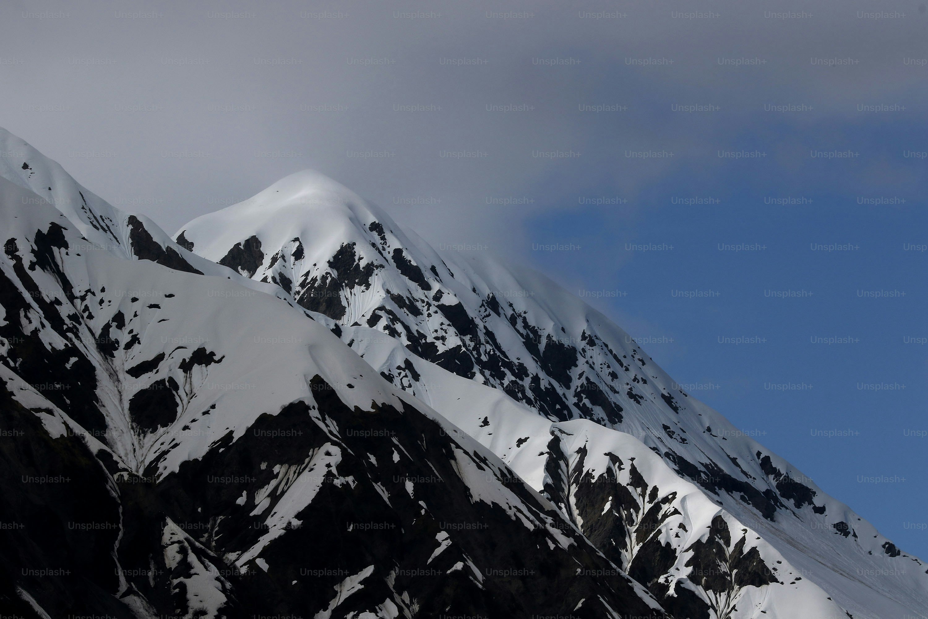 a mountain covered in snow under a cloudy blue sky