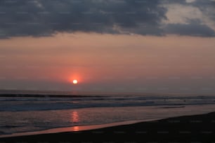 the sun is setting over the ocean on a cloudy day