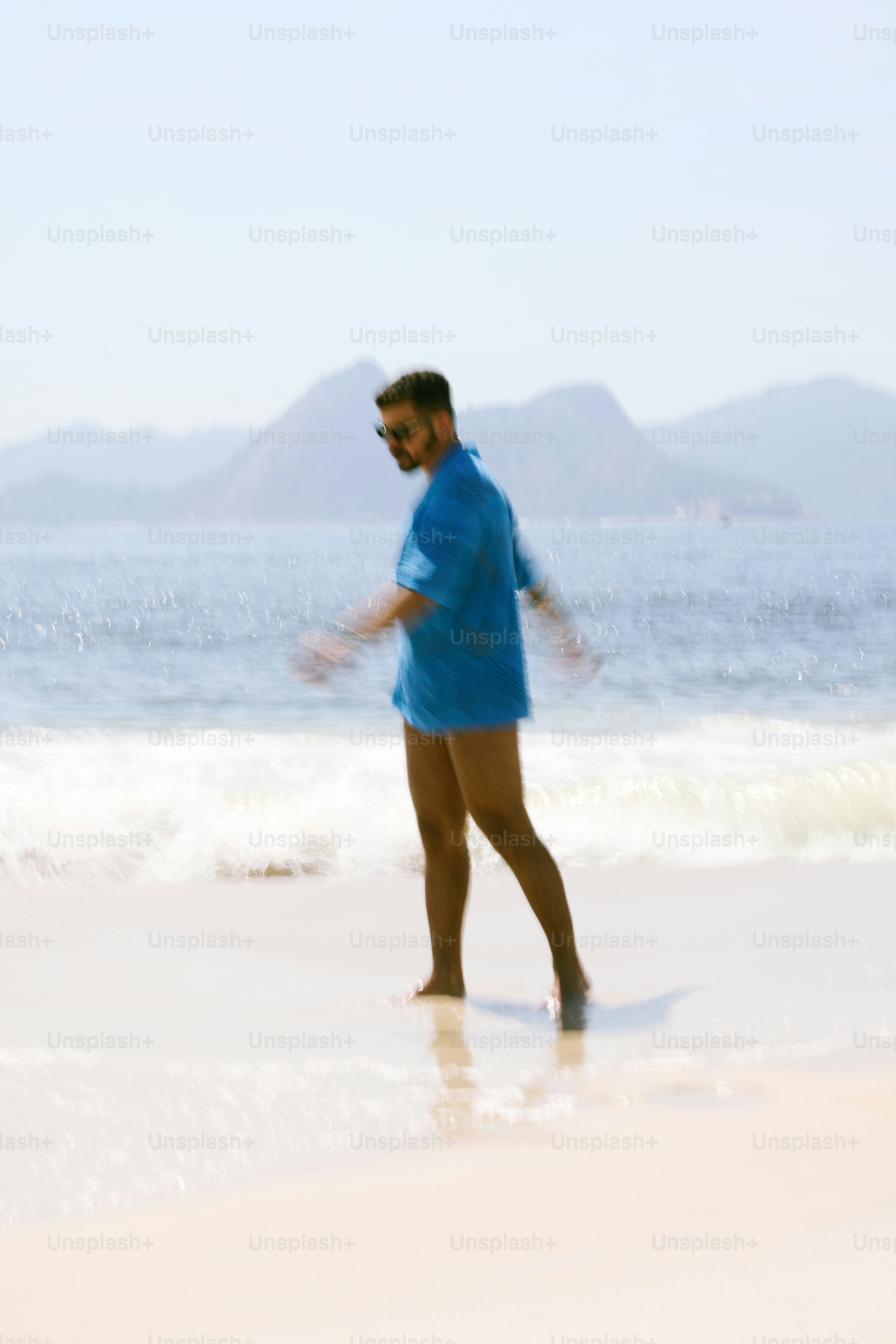 a man in a blue shirt is walking on the beach