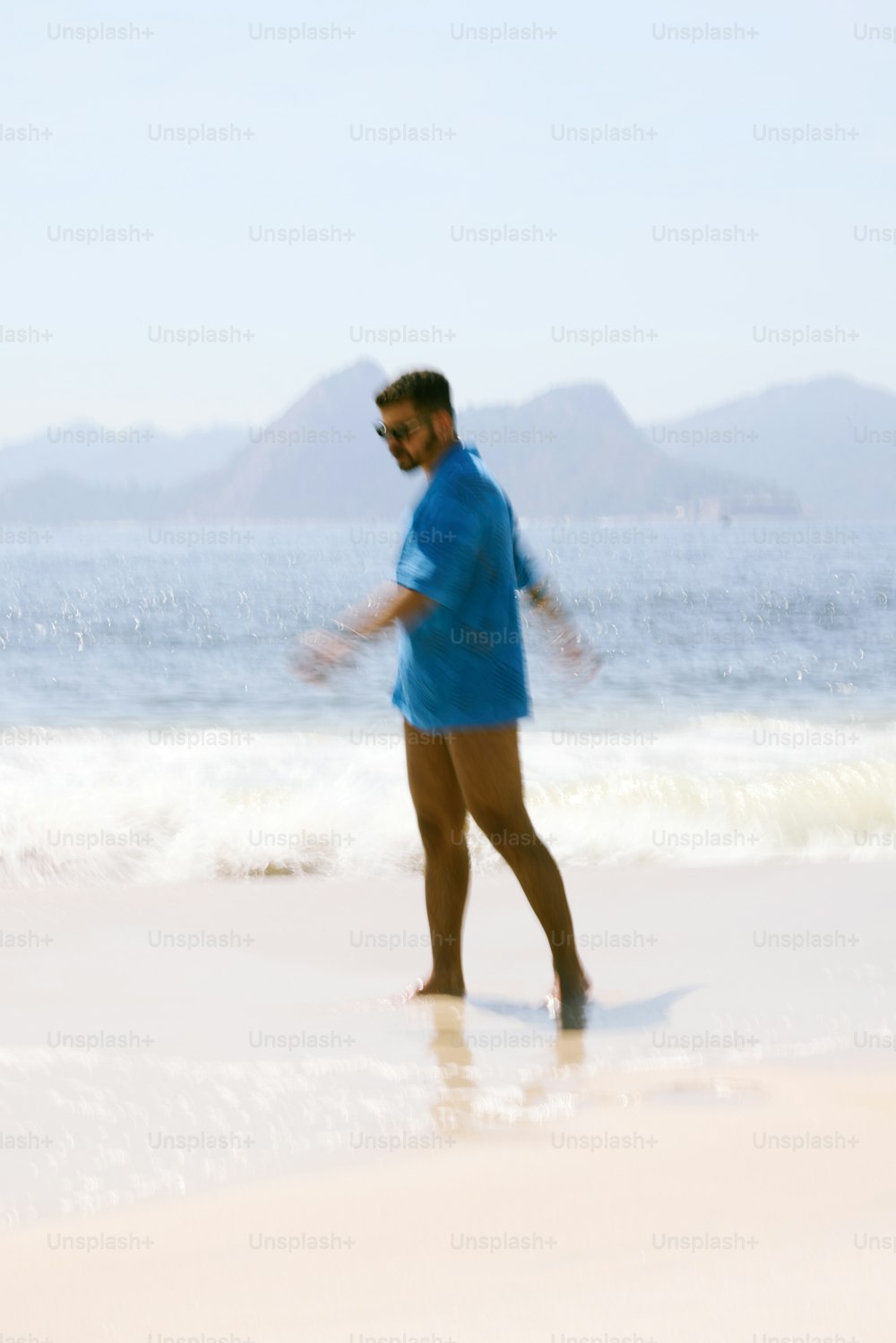 a man in a blue shirt is walking on the beach