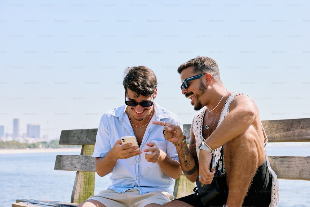 two men sitting on a bench looking at a cell phone