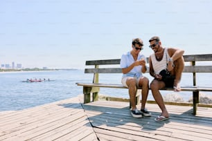 two men sitting on a bench looking at a cell phone