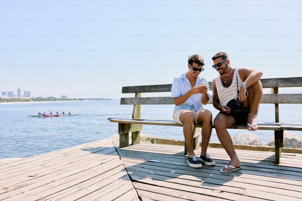 two men sitting on a bench looking at a cell phone