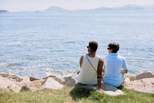 two people sitting on a rock looking out at the water