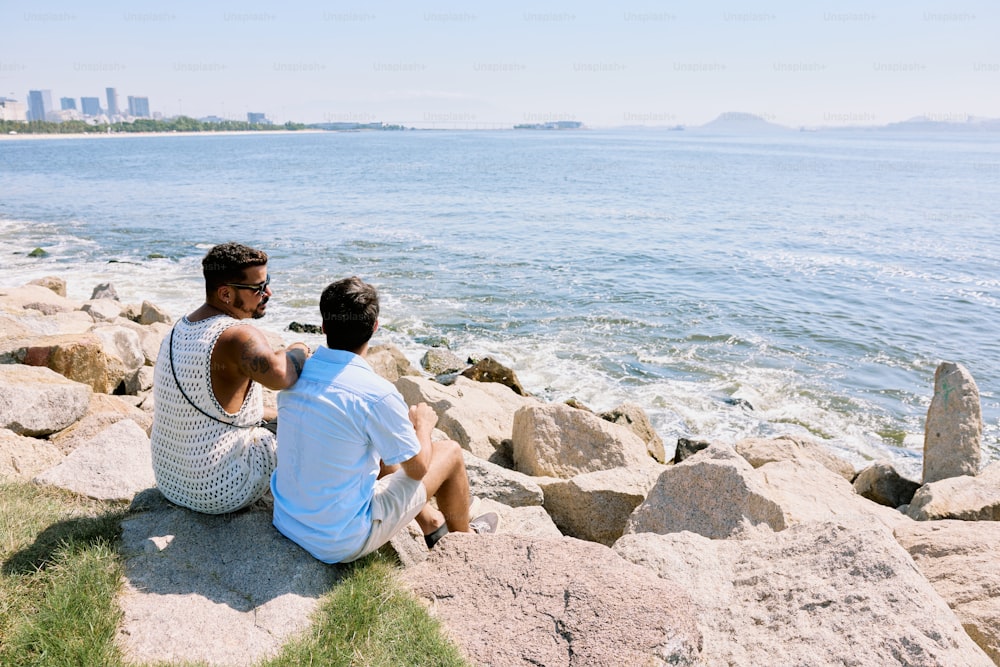two people sitting on rocks near the water