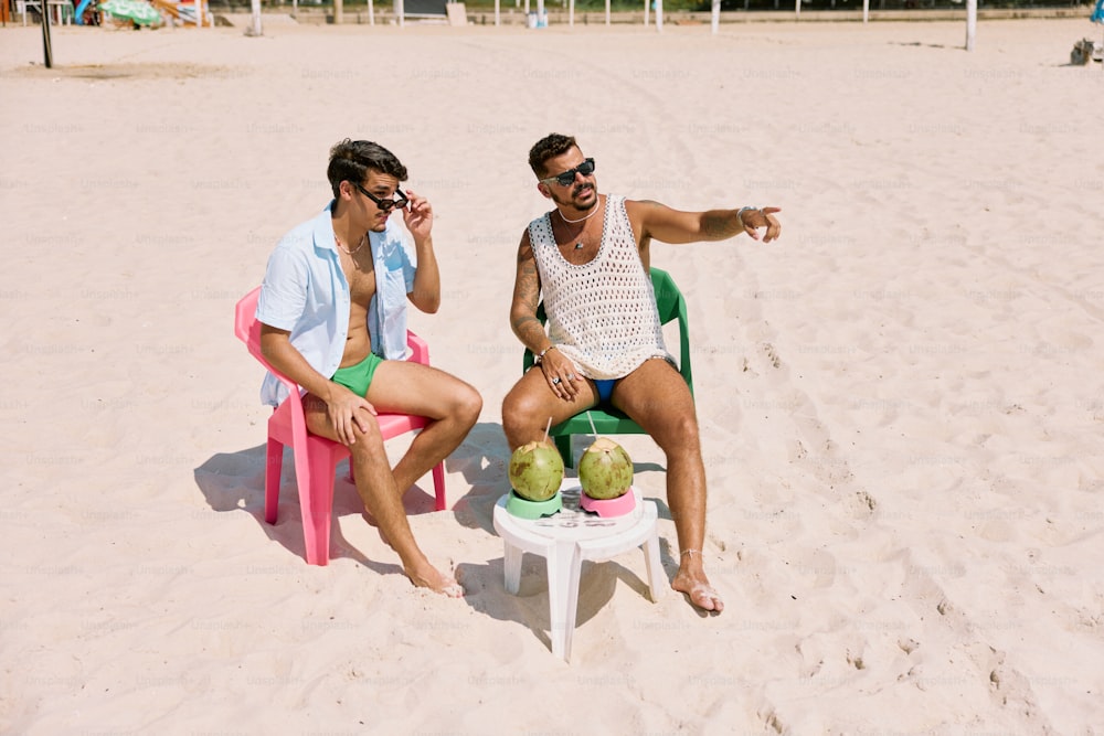 two men sitting in lawn chairs on a beach