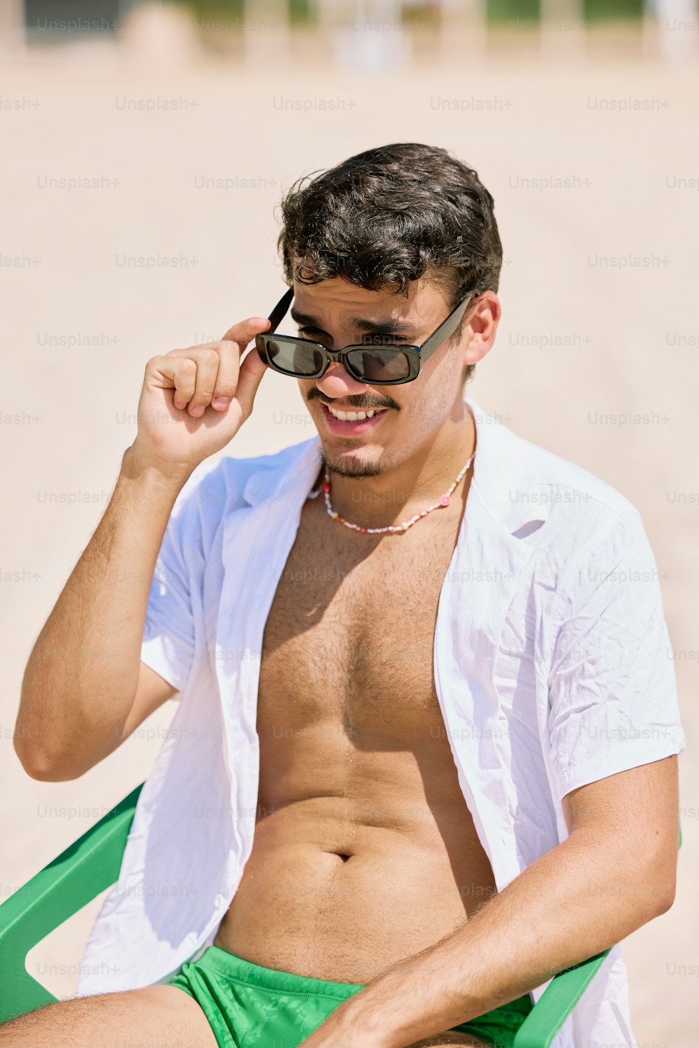 a shirtless man sitting on a chair on the beach