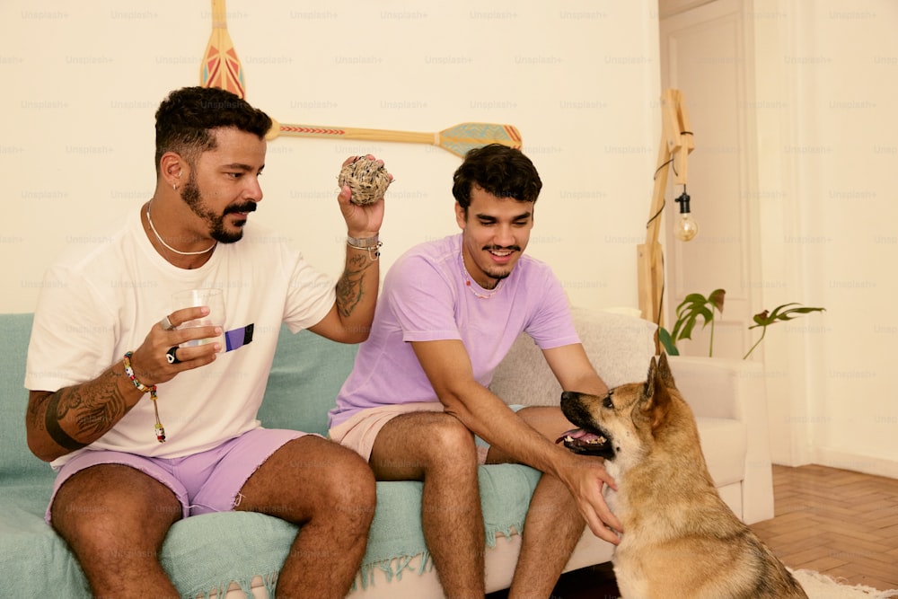 a couple of men sitting on top of a couch next to a dog