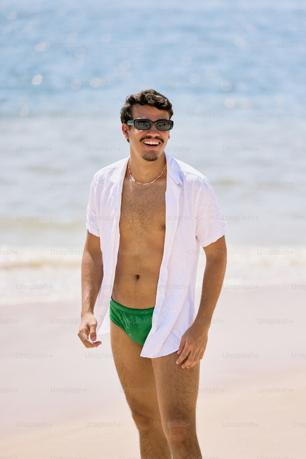 Un hombre con camisa blanca y pantalones cortos verdes en la playa