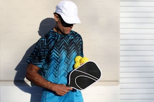 a man holding a bag of tennis balls and a racquet