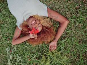 a woman laying on the grass with a flower in her hand