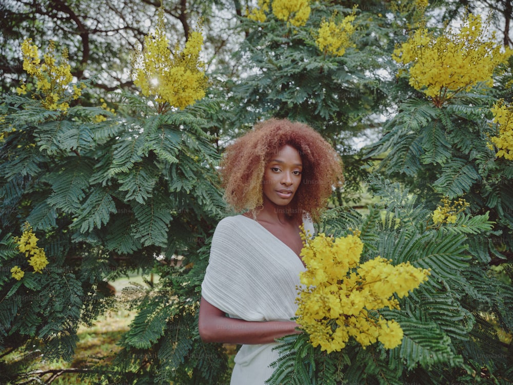 a woman standing in front of a bush with yellow flowers